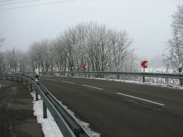 Een Verkeersweg Met Richtingaanwijzers Langs Bladloze Bomen Bedekt Met Sneeuw — Stockfoto