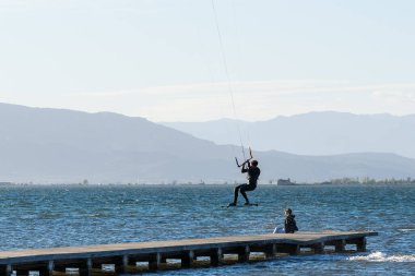 A beautiful view of a Kitesurfer at Playa del Trabucador jumping over a wooden bridge clipart