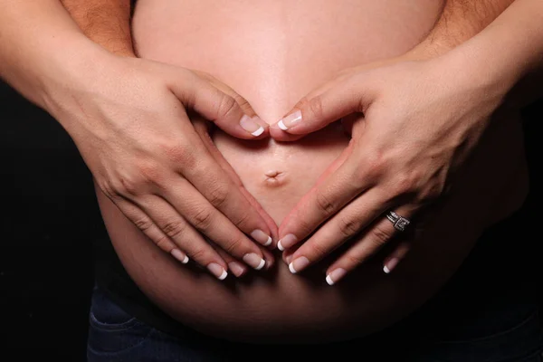 心臓の形で男性の手に彼女の手で妊娠中の女性の腹 — ストック写真