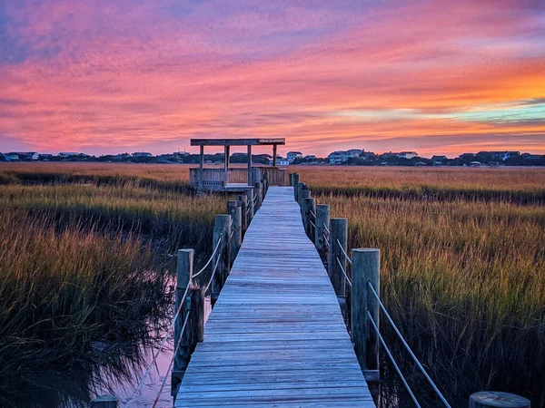The beautiful scenery of a boardwalk in the meadow with a sunset background