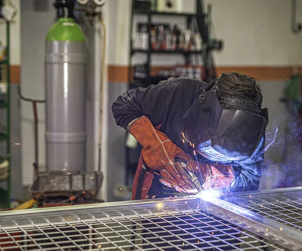 Professional welder with face protection mask welding a door in the workshop. Blacksmith work concept.