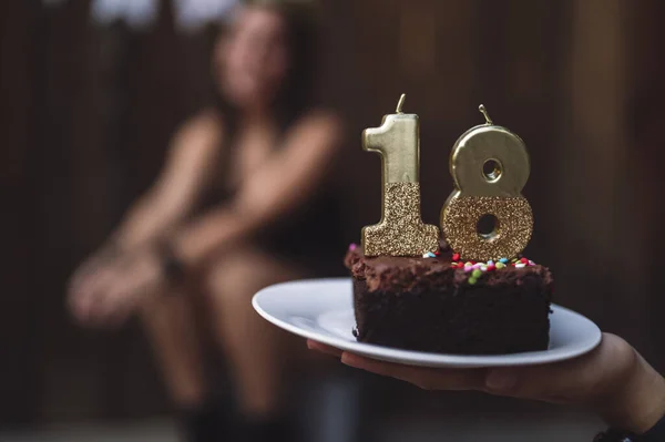 A hand holding a plate with a slice of cake and number 18 candles