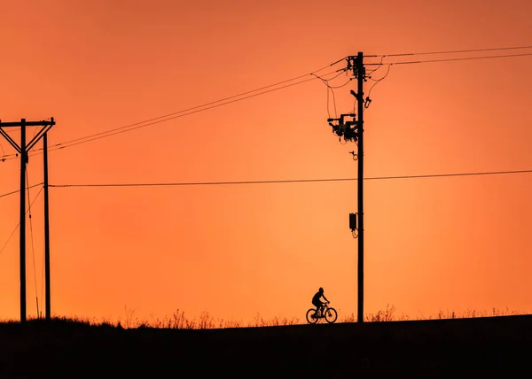 黄昏时分 一个骑自行车和电线杆的男人在橙色天空中的轮廓 — 图库照片