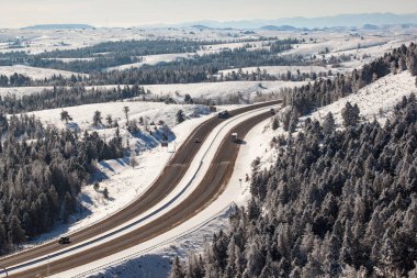 An aerial shot of winter roads lined with snow and alpine trees along I-80 in southern Wyoming clipart
