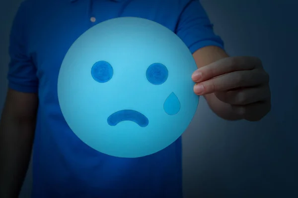 A hand holding a blue sad face sign - the blue Monday concept