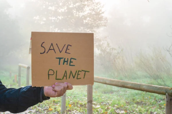 男性の手は 背景に森と地球を救うというスローガンと段ボールサインを保持しています — ストック写真