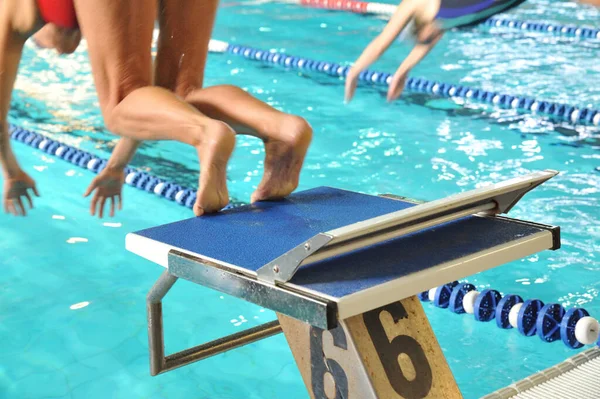 A close-up shot of human legs on the starting block of the swimming pool ready to jump
