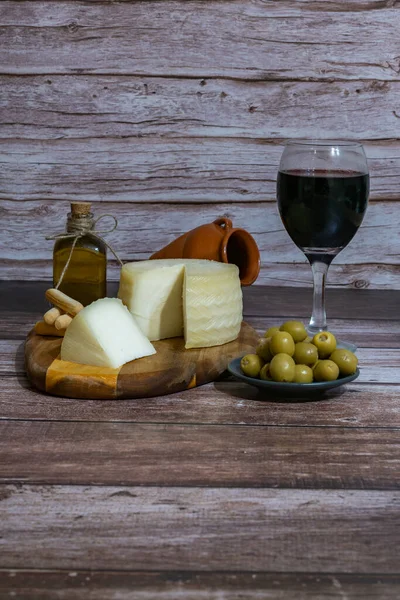 cured cheese cut with a glass of red wine, stuffed olives and extra virgin olive oil on a wooden table copy-space