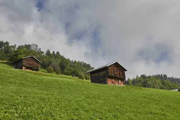 Pair Small Wooden Houses Steep Bright Green Hill Surrounded Lush — Stock Fotó