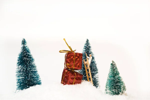 A miniature figure painter painting red gift packages in a snowy area with fir trees