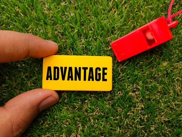 A Whistle and colored board written with text ADVANTAGE on a green grass background. Sport and football concept