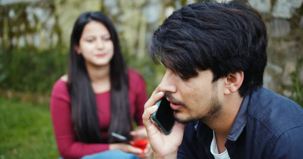 A shallow focus of a young adult Indian man talking on the phone during a party in a garden