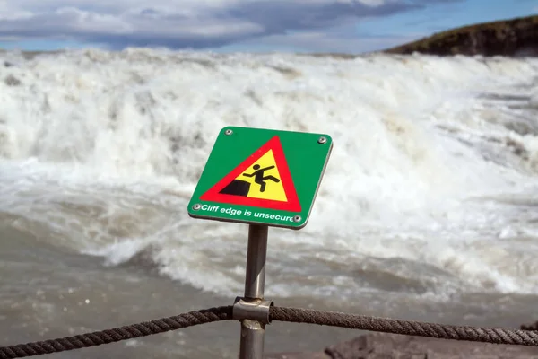 川の背景に白い波がある警告標識があります — ストック写真