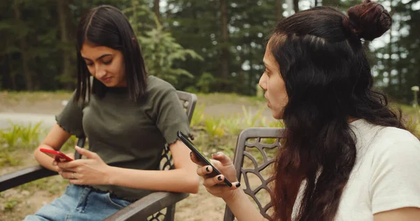 Две Молодые Женщины Пользуются Смартфоном Разговаривают Мобильному Телефону Сидя Скамейке — стоковое фото