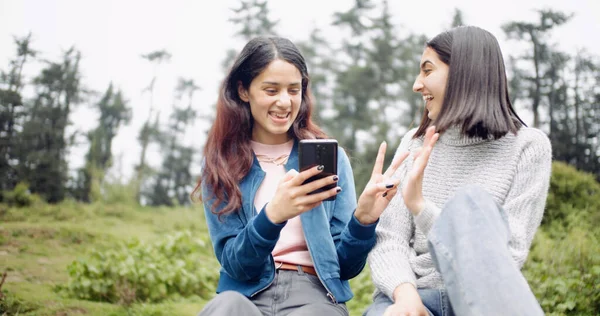Two Young Women Using Smartphone Smiling While Sitting Grass Looking — Stockfoto