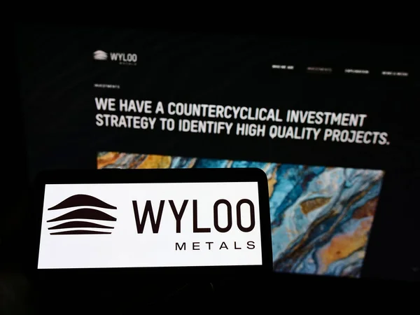 手握智能手机在电脑屏幕前 其符号为Wyloo Metals公司的网站 — 图库照片