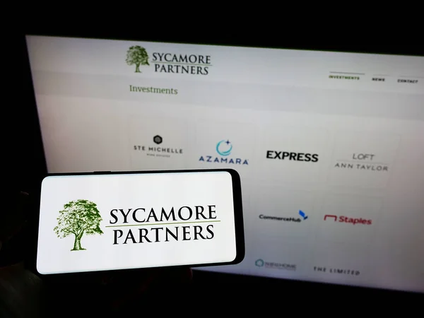 手握智能手机在电脑屏幕前 其符号为Sycamore Partners — 图库照片