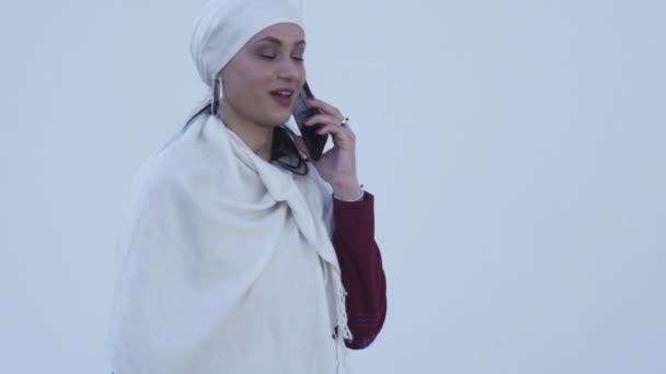 一个穿着白色头巾的穆斯林美女在城市的背景下打电话 — 图库视频影像