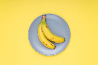 2 bananas on a gray plate. yellow background