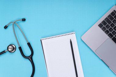 black stethoscope, laptop, notepad and pen, blue isolated background
