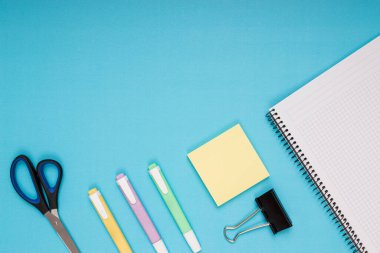 Notebook, scissors, colored pencils, note paper and clamp. back to school. Isolated blue background