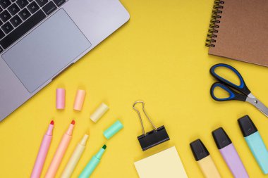 Laptop, scissors, clamp, notepad, colored pencils. back to school. Isolated yellow background