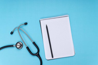 black stethoscope, notepad and pen, blue isolated background