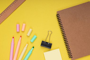 Notebook, colored pencils, note paper and clamp, ruler. back to school. Isolated yellow background