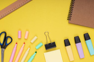 Notebook, scissors, colored pencils, ruler, note paper and clamp. back to school. Isolated yellow background