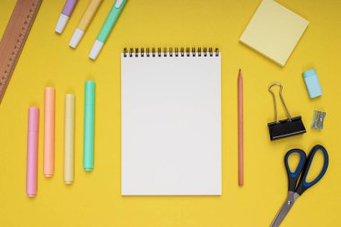 notepad, scissors, pencil, sharpener, ruler, eraser, colored pencils, clips and note paper. back to school. Isolated yellow background