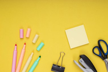 Colored pencils, clips and note paper, scissors, staple. back to school. Isolated yellow background