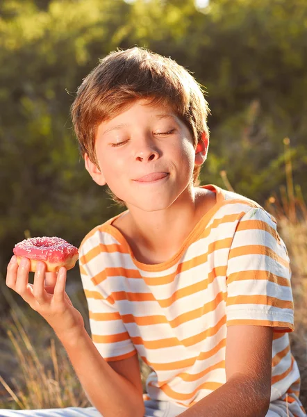 Jonge jongen eten donut buitenshuis — Stockfoto