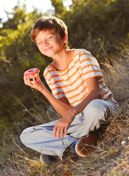 Usměvavý chlapec jíst koblihy — Stock fotografie