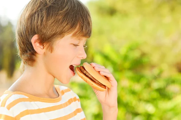 Child biting hamburger outdoors — Stock Photo, Image