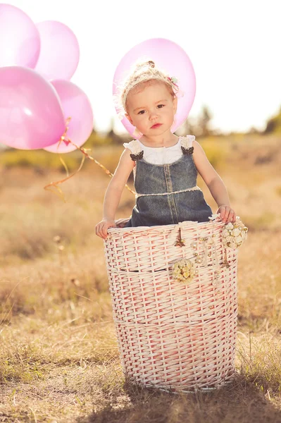 Baby girl playing in basket with balloons — Stock Photo, Image