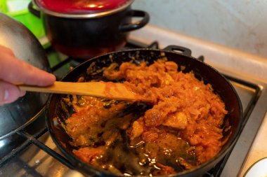 Tahta kaşığı karıştıran bir adam kızartma tavasında bir et tabağı