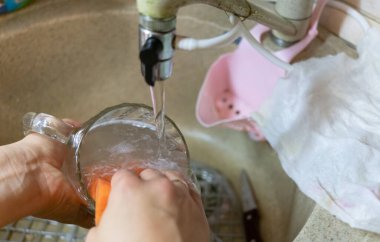 Kadın bardağını lavaboda akan suyun altında yıkıyor.