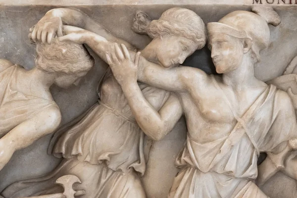 在大理石墙上雕刻的雕像的特写中 一个古罗马士兵用头发抓住一个女孩 而另一个女孩则试图保护她 — 图库照片