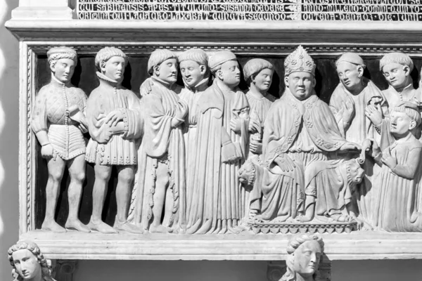 Black and white photo of sculptures of men surrounding bishop,carved in the marble exterior facade of catholic church in Naples, Italy