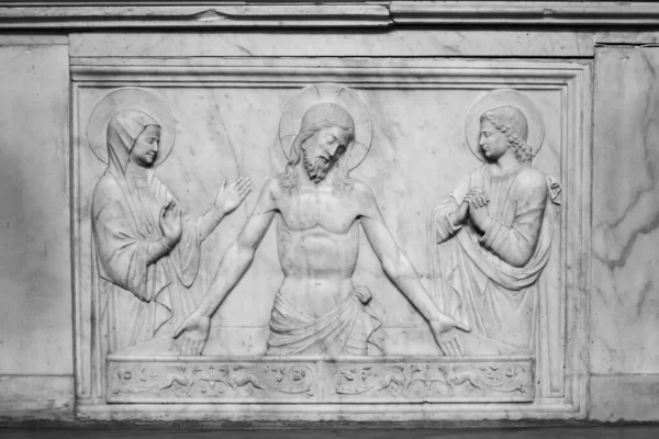 Black and white photo of religious sculptures carved on a marble wall showing Jesus between Virgin Mary and another catholic saint