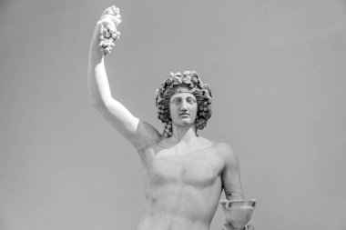 Black and white photo of ancient roman statue representing young god Bacchus with bare torso