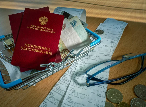 Pension certificates, Russian money, sales receipts, a shopping basket and glasses are on the table. Conceptual background with Russian pensioner documents and rubles.