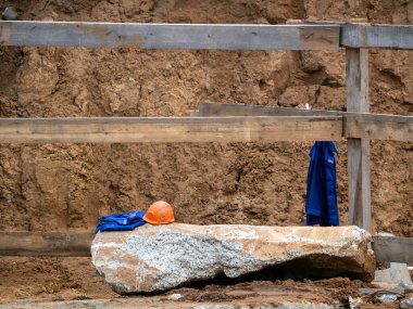 İşçilerin bıraktığı tulumlar. Ceket ahşap bir tahtada asılı. Miğfer ve giysiler büyük bir taşın üzerinde. Üniformalı iş geçmişi.