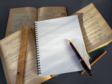 Açık kitaplar masanın üzerinde düzensizce yatar. Yukarıda açık bir defter var. Kalem boş bir sayfada. Üniversite eğitimi kavramı. Akademik bilimler okuyorum. Bilimsel çalışma, tez yazma.