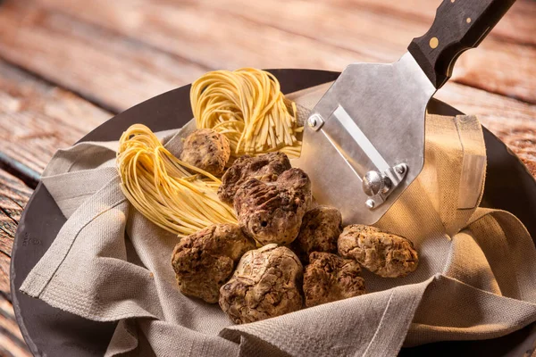 Alba white truffles in napkin with raw egg tagliolini and steel truffle cutter on wooden background