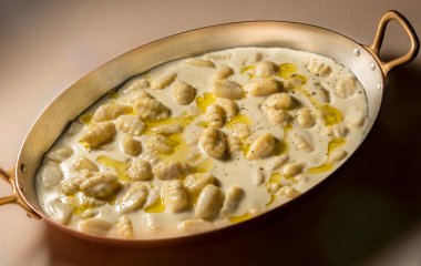 Oval bakır kapta kastelmagno peyniri soslu İtalyan gnocchi.