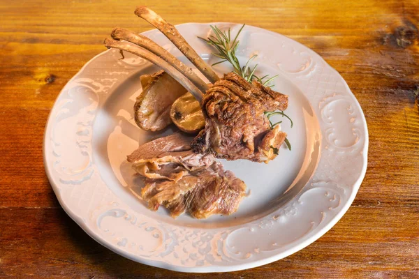 Patatesli kuzu pirzolası ve ahşap masada beyaz tabakta biberiye, sıcak ışık, üst manzara.