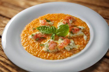 Domates soslu risotto Mazara del Vallo kırmızı karidesleri, mozzarella burrata peyniri ve fesleğen yaprakları ahşap masada beyaz tabakta.