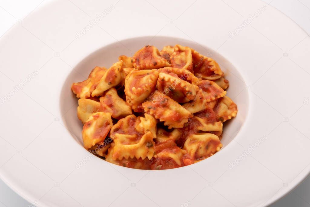 Typical agnolotti del plin, stuffed egg pasta ravioli from Langhe, Piedmont, Italy, seasoned with tomato sauce in white dish