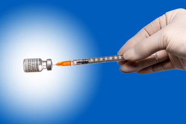 Torino, İtalya - 18 Aralık 2021: Pfizer-BioNTech COVID-19 Aşı Comirnaty şişeleri, lateks eldivenli şırınga aşısı dozunu mavi arkaplandaki orijinal aşı şişelerinden alan